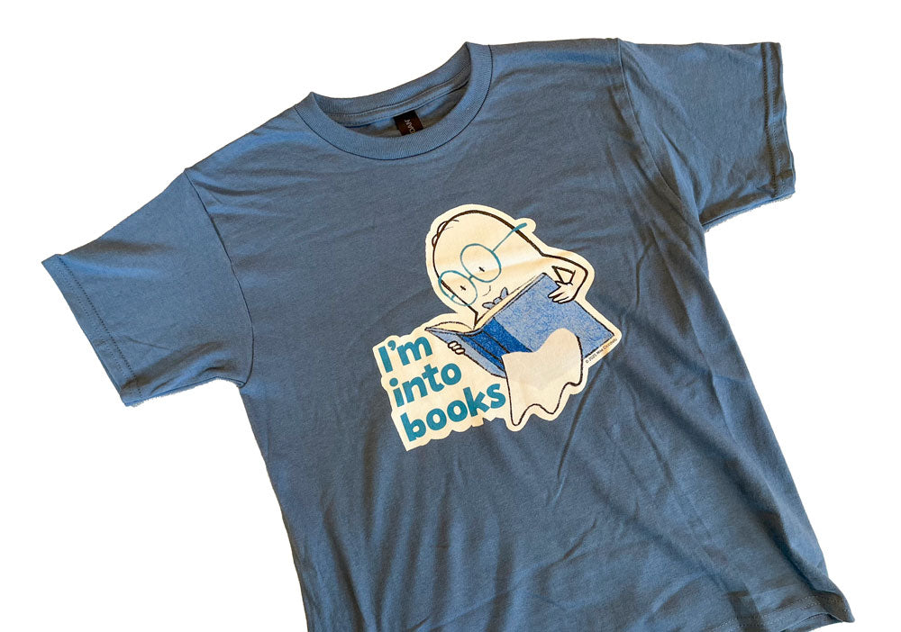 Indigo Blue t-shirt with a ghost character holding a book while reading it. The ghost is floating through the book. "I'm into Books" text appears next to the character on a white background.